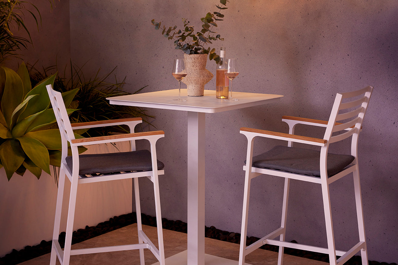 Outdoor bar furniture with two high aluminium bar stools and a bar table set with wine, in a modern concrete outdoor setting.