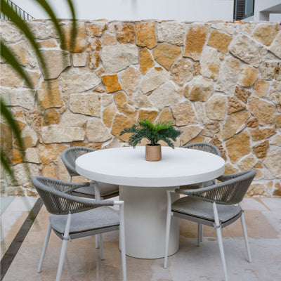 Four contemporary outdoor dining rope chairs with sleek, minimalist designs, paired with a white round outdoor dining table. The outdoor furniture is arranged in a backyard, with a backdrop of a rocky sandstone wall.