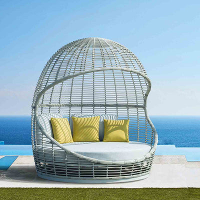 A stylish wicker daybed with bright yellow pillows, set poolside in a modern home's outdoor area, perfect for outdoor living.