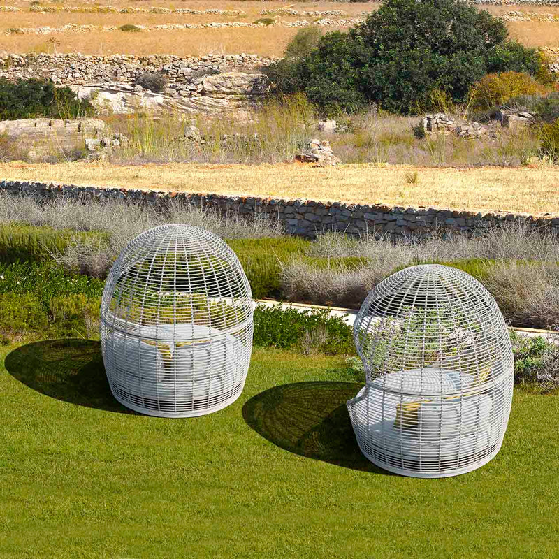 Two elegant wicker daybeds on a grassy lawn outside a grand European house, basking in the warm sunlight, ideal for outdoor living.