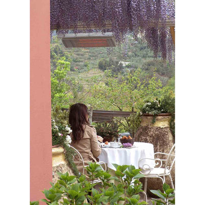 Woman enjoying a meal outdoors, surrounded by greenery, with a white Heatscope heater overhead providing warmth for comfortable outdoor living.