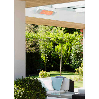 White Heatscope heater installed above a lounging area outdoors, with sunny weather and lush greenery in the background, perfect for outdoor living.